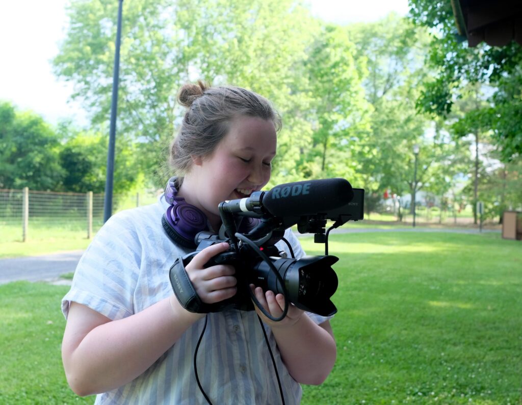 Women with brown hair in a bun uses a video camera to film